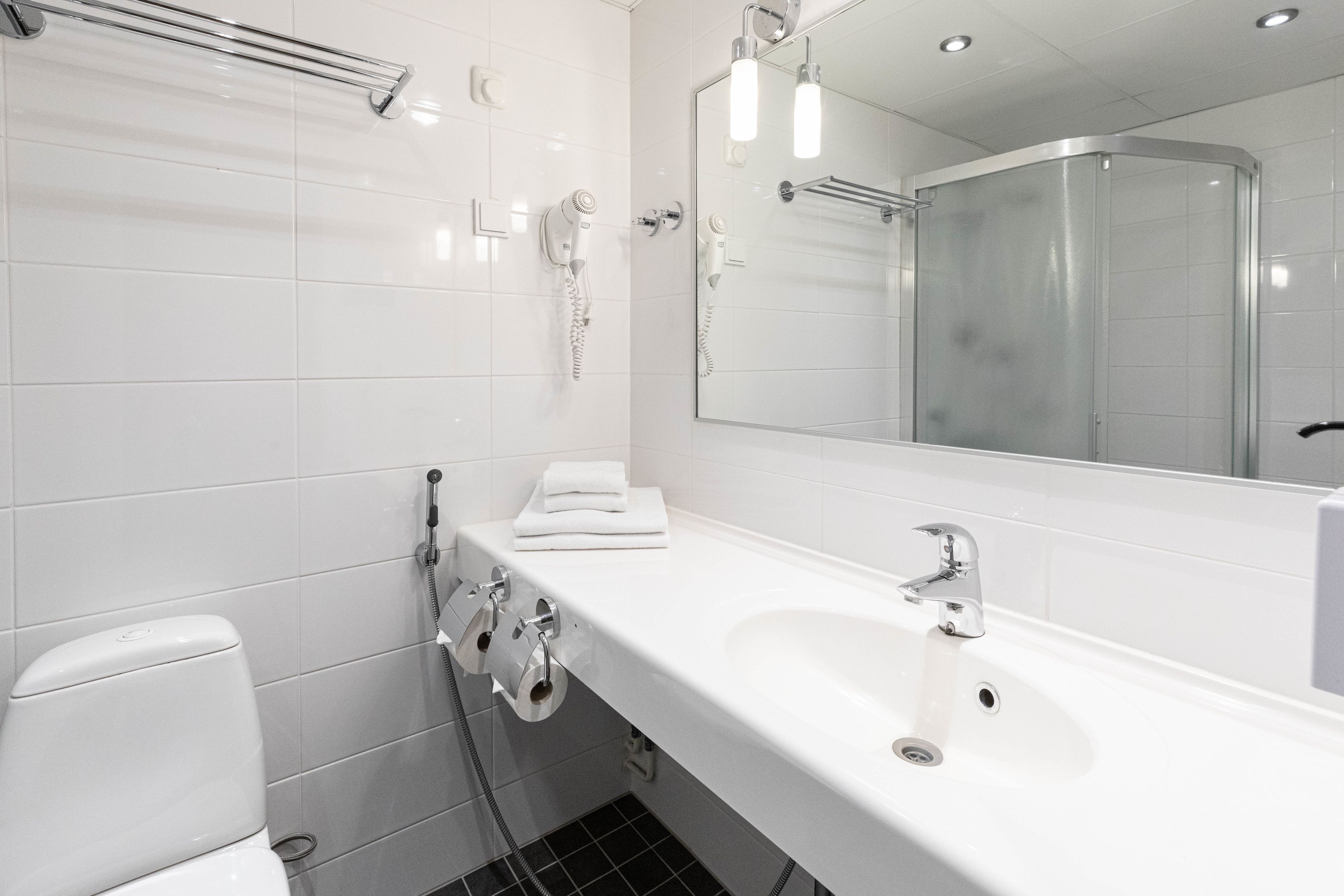 Een moderne badkamer met een wit wastafelmeubel, een spiegel, een handdoekhouder en een douchegedeelte.