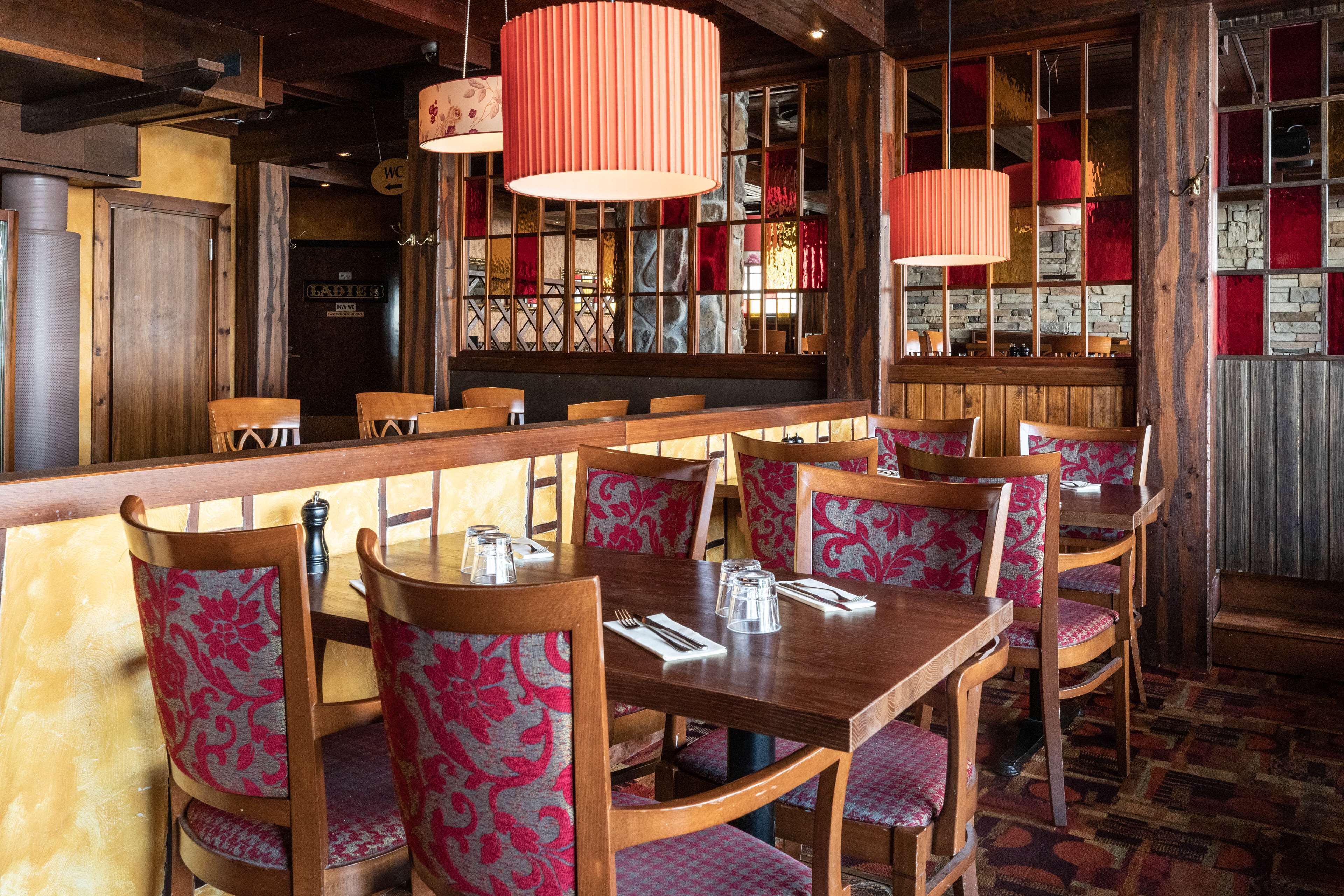 A restaurant with wooden tables and chairs, a bar area, and a patterned wall.