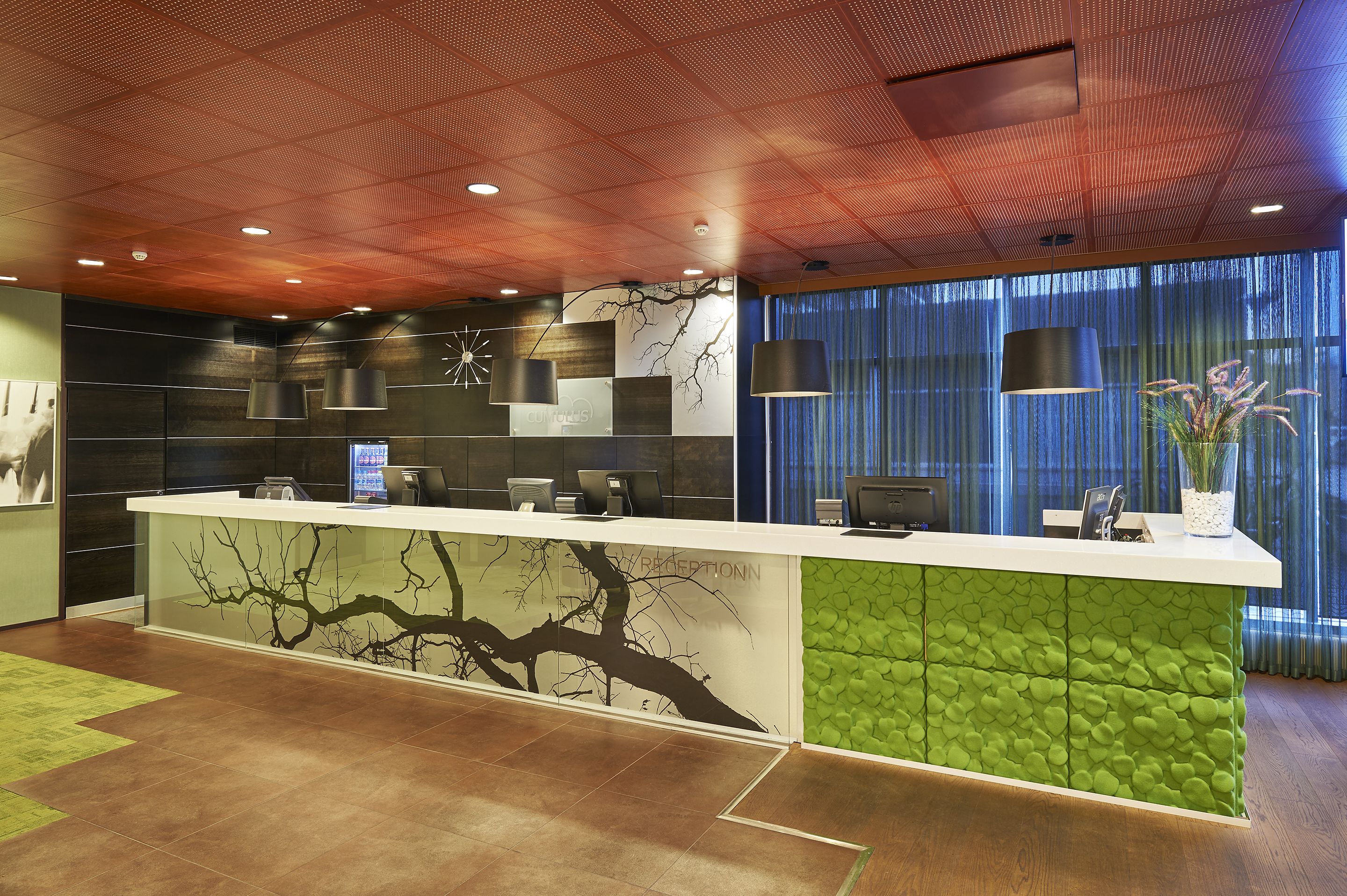 A reception area with a modern design, featuring a reception desk, wall-mounted lamps, and a large window with curtains.