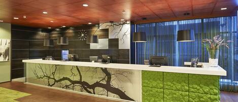 A reception area with a modern design, featuring a reception desk, wall-mounted lamps, and a large window with curtains.