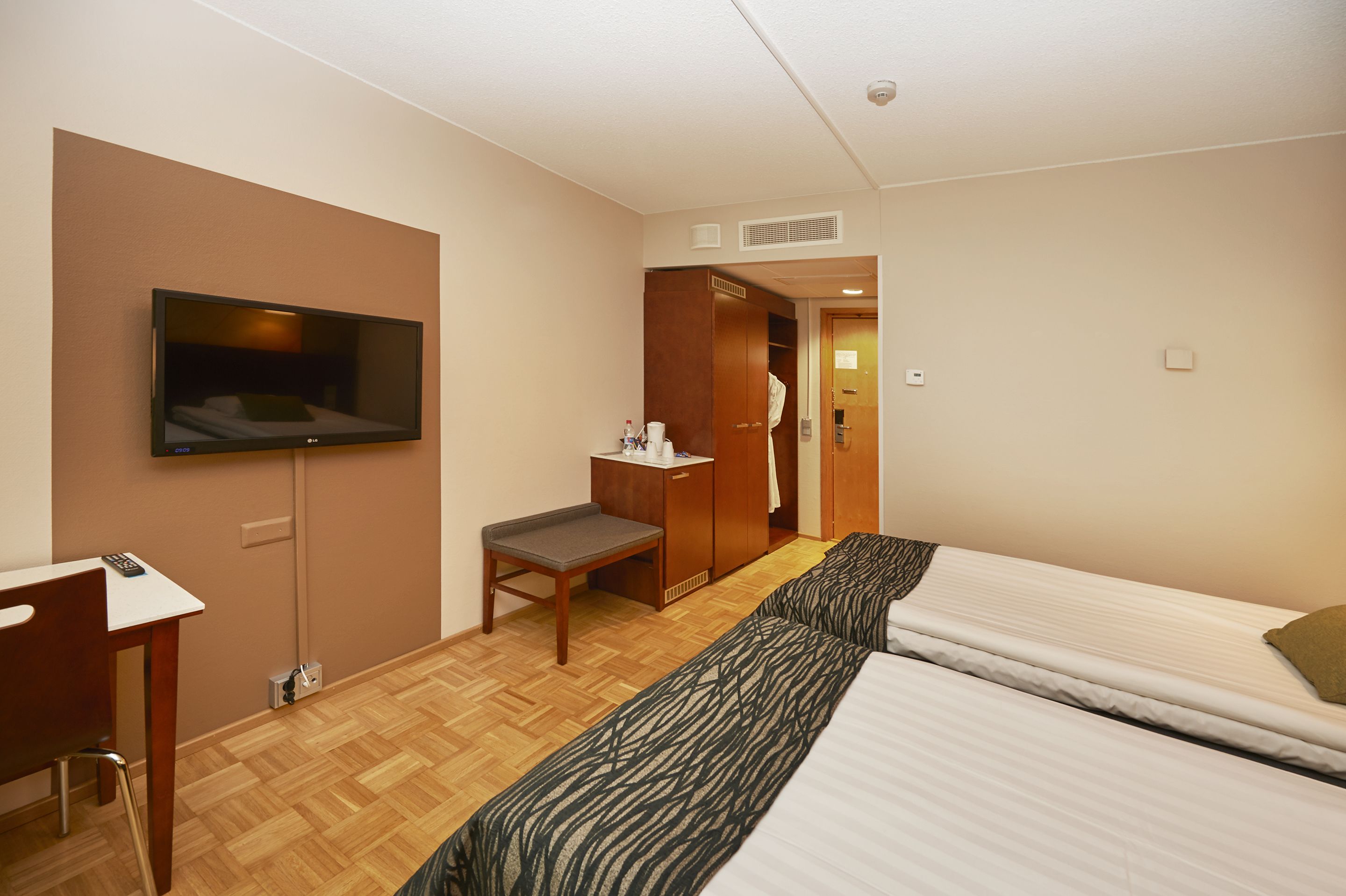 Una habitación de hotel con cama, escritorio, silla, televisor y armario.