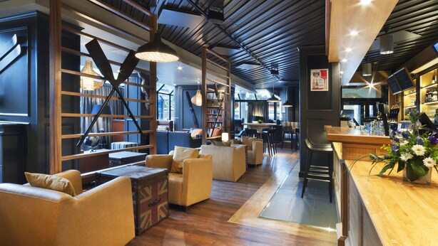 A modern bar area with wooden furniture, a bar counter, and a bookshelf. - Scandic Jyväskylä City (Jyväskylä)