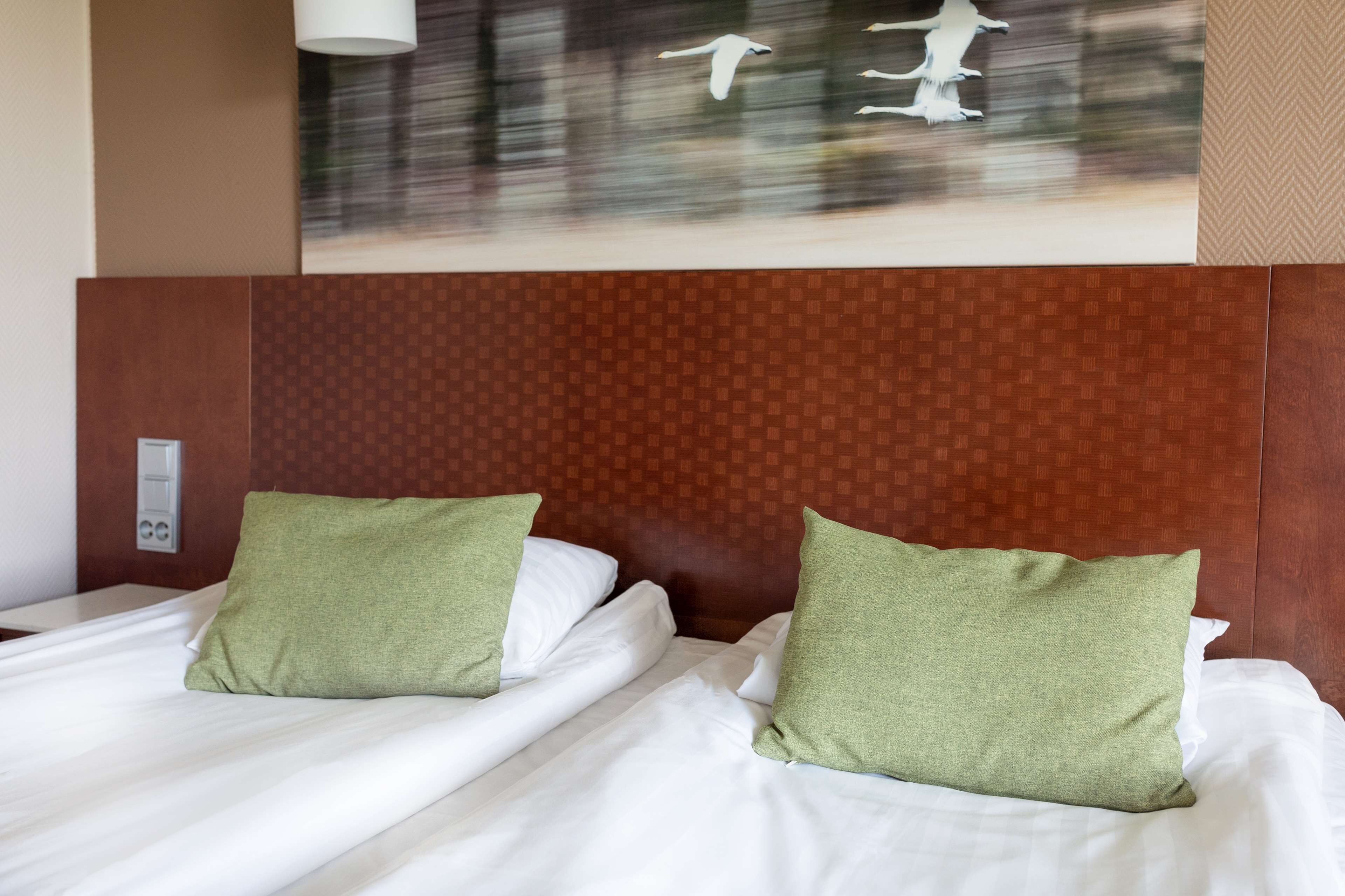 A hotel room with two beds, each with green pillows and white linens.