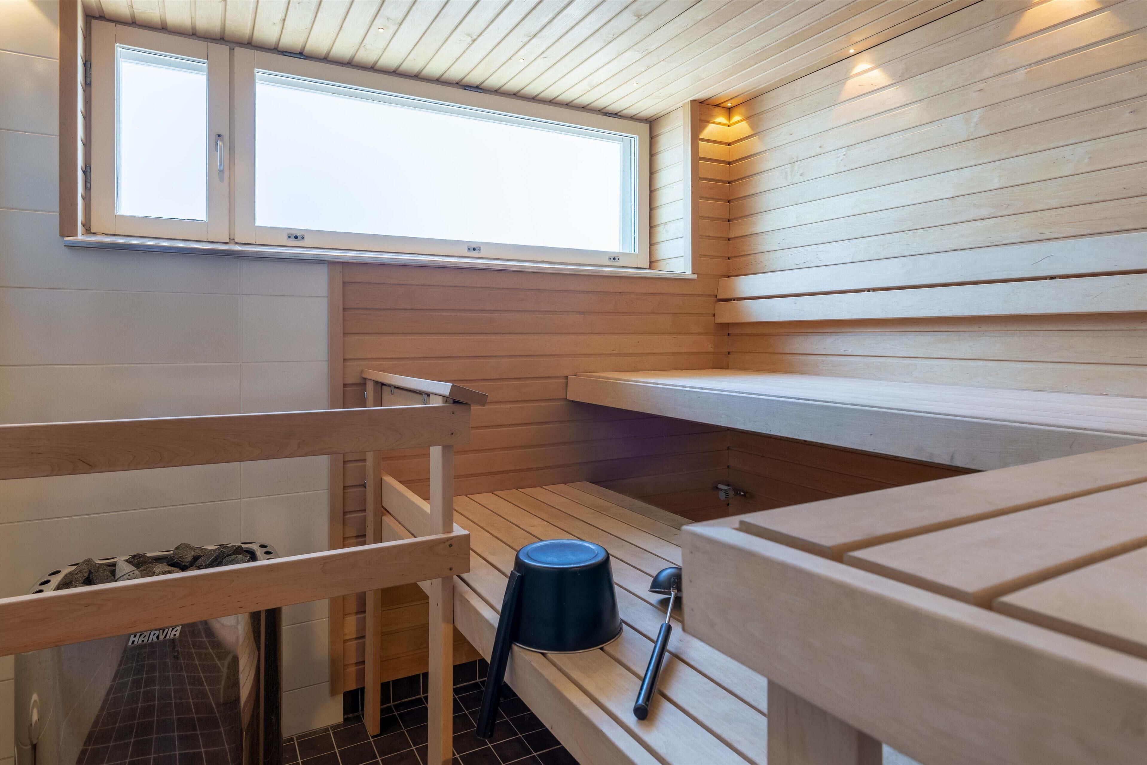 A sauna with wooden walls and benches, a window, and a sauna bench with a towel and a bottle.