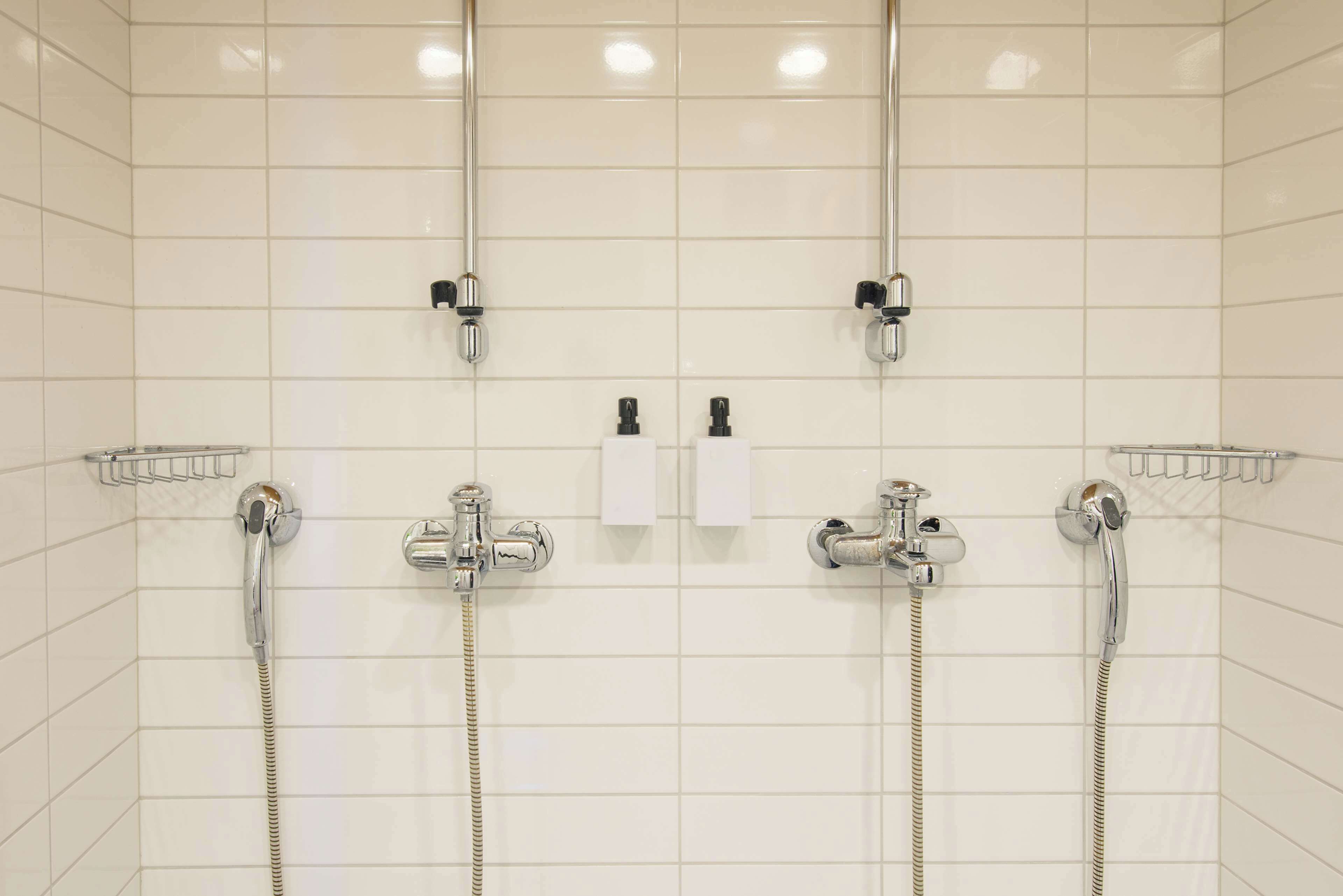 Un baño con tres cabezales de ducha, un perchero y un dispensador de jabón.