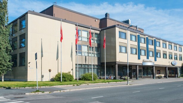 A modern building with a beige facade, multiple windows, and a sign indicating it is a hotel.
