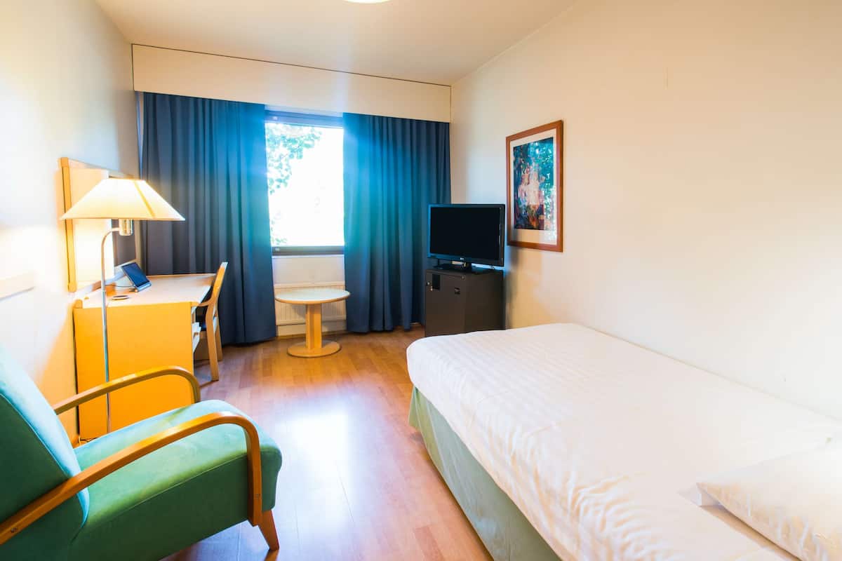 A hotel room with a bed, a desk with a lamp, a television, and a painting on the wall.