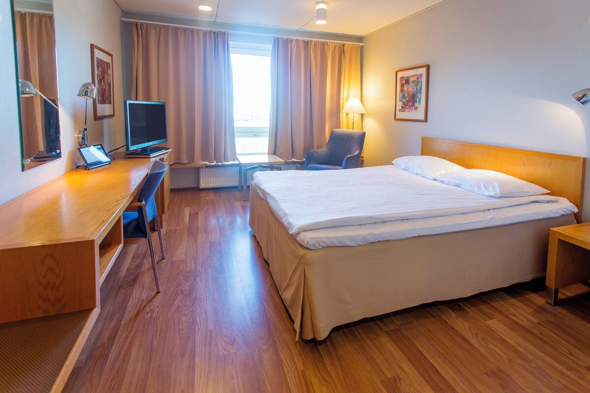 A hotel room with a bed, desk, chair, television, and a window with curtains.
