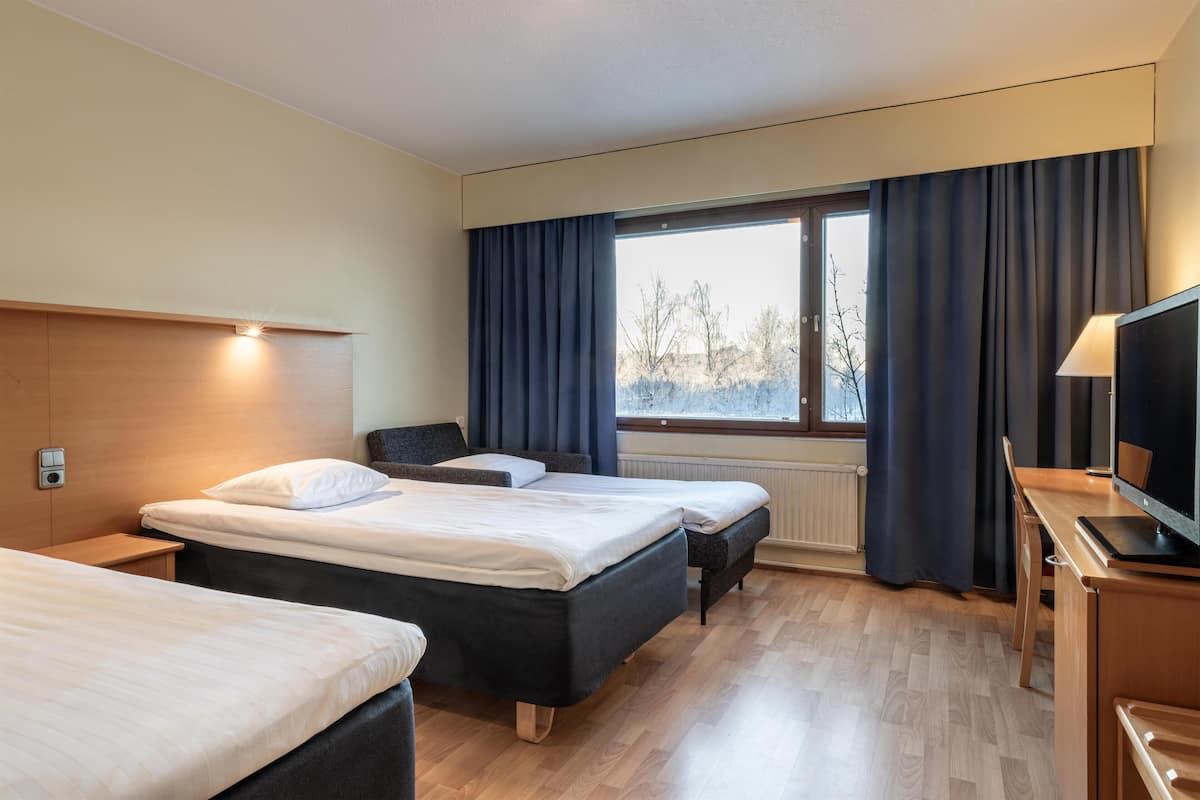 A hotel room with two beds, a desk with a computer, a TV, and a window with curtains.