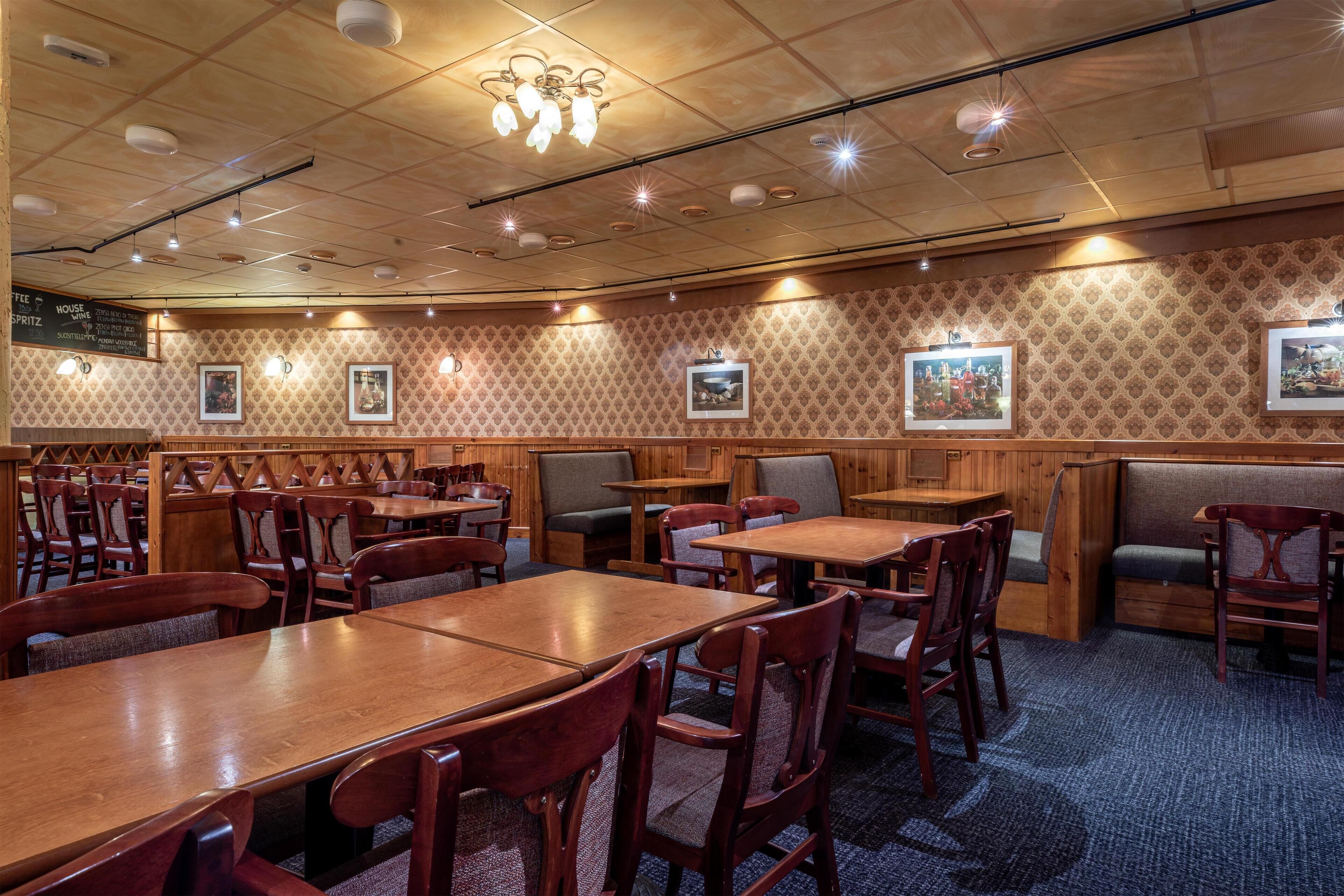 A restaurant with wooden tables and chairs, a patterned wall, and framed pictures.