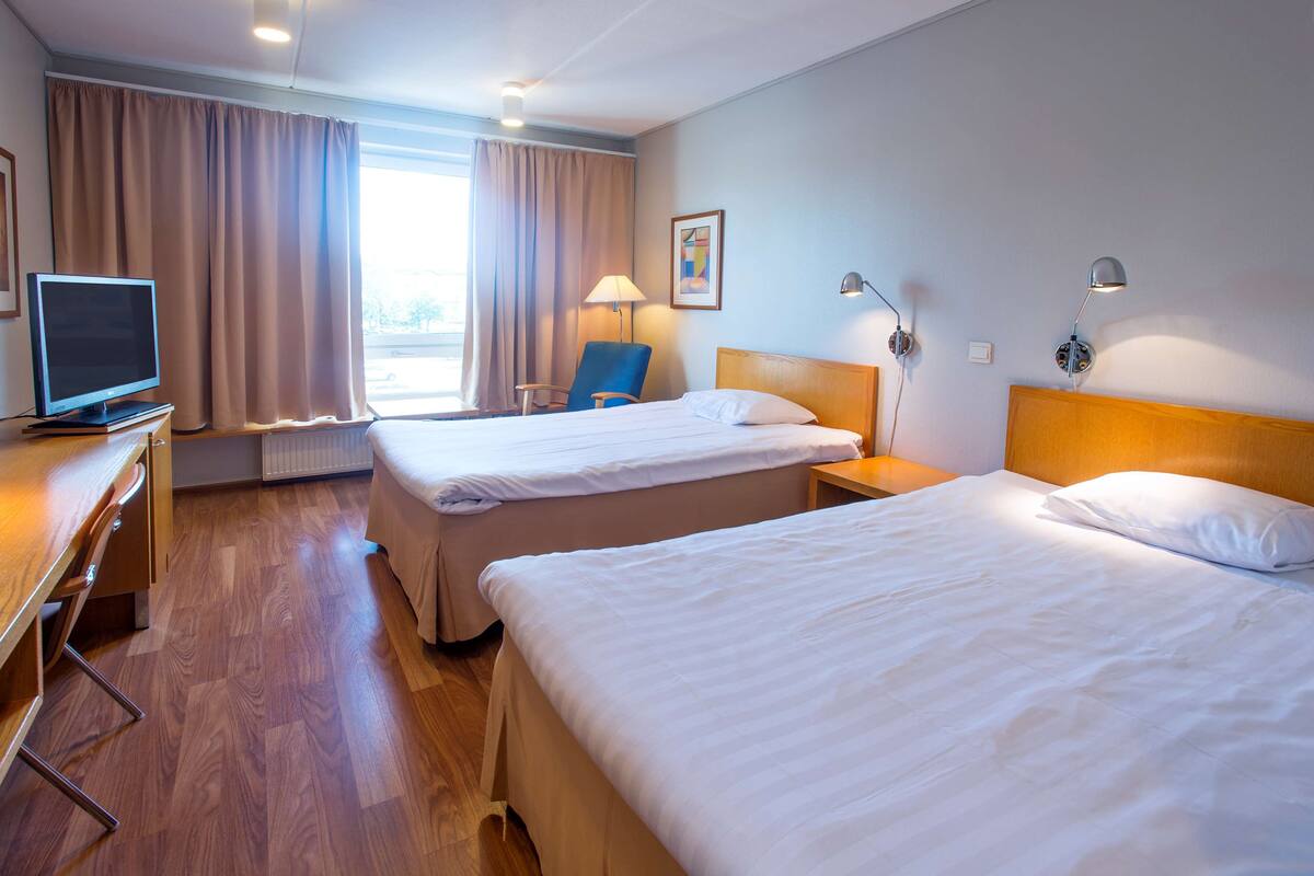 A hotel room with two beds, a desk with a television, and a chair.