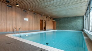 An indoor swimming pool with wooden panel walls, tiled floor, and a clear view of the pool area.