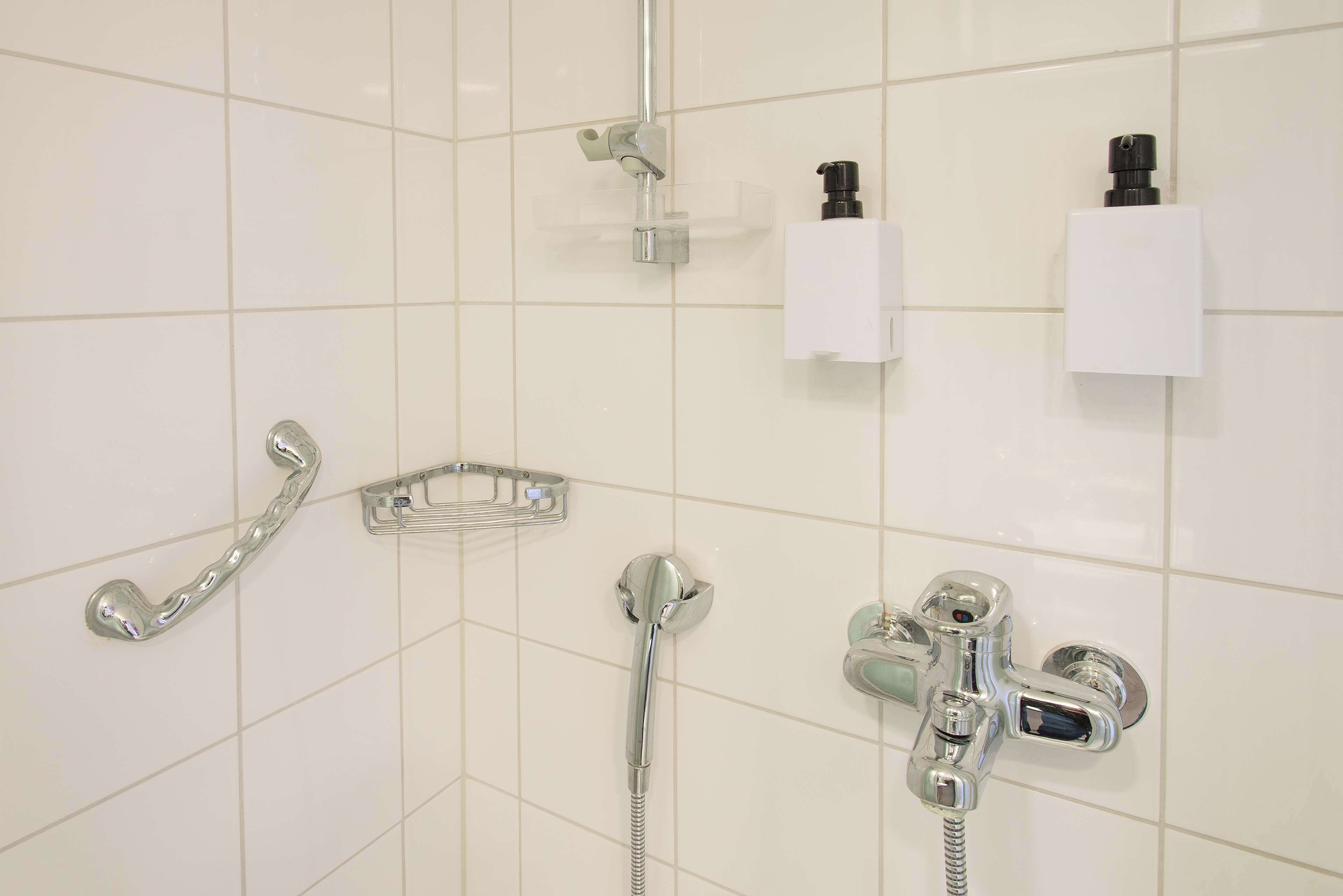 A bathroom with a shower, a hand dryer, and a soap dispenser on the wall.