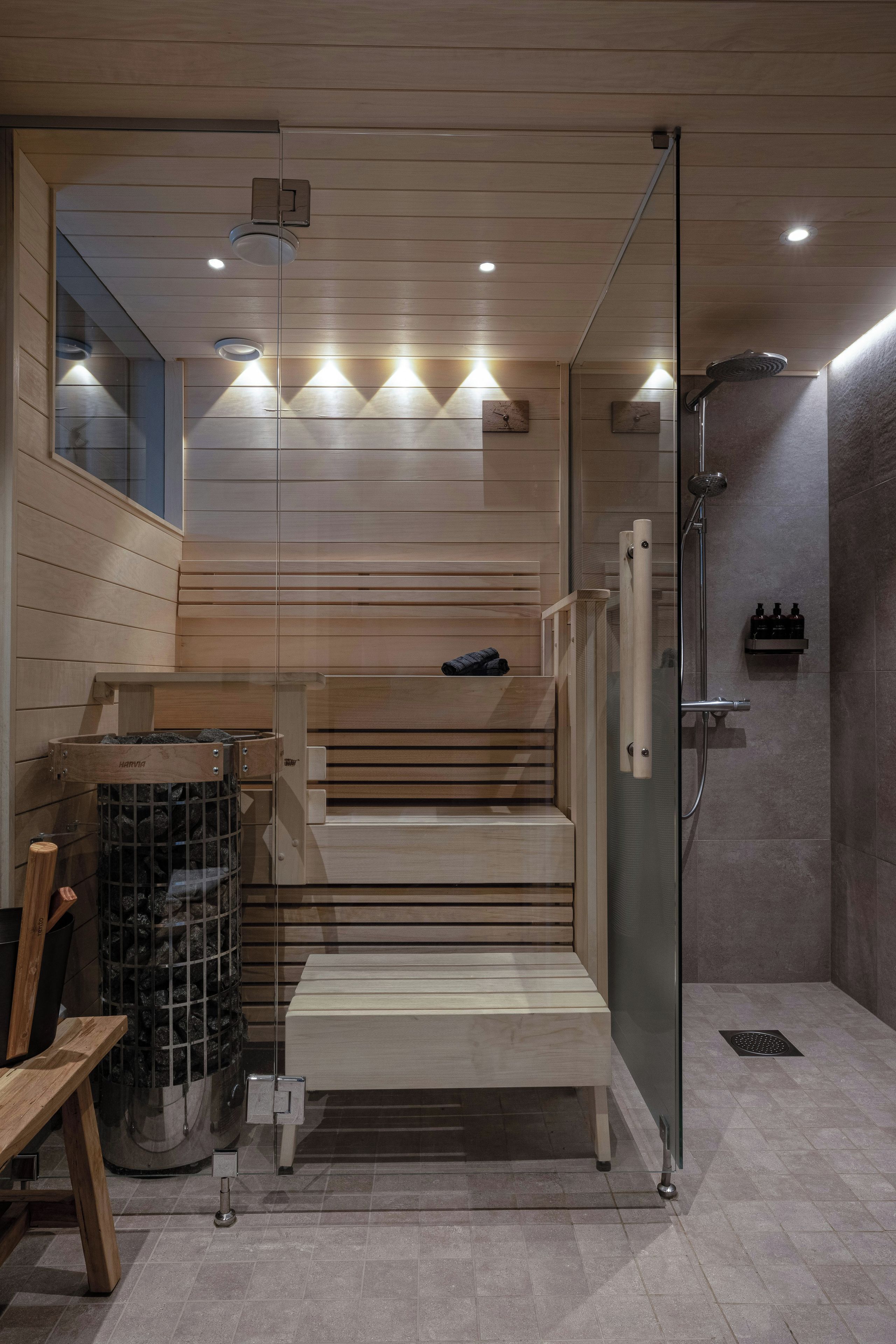 Un baño moderno con cabina de ducha de vidrio, escalones de madera y un banco.