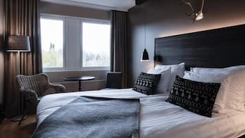 A hotel room with a bed, a chair, a small table, a lamp, and a window with curtains.