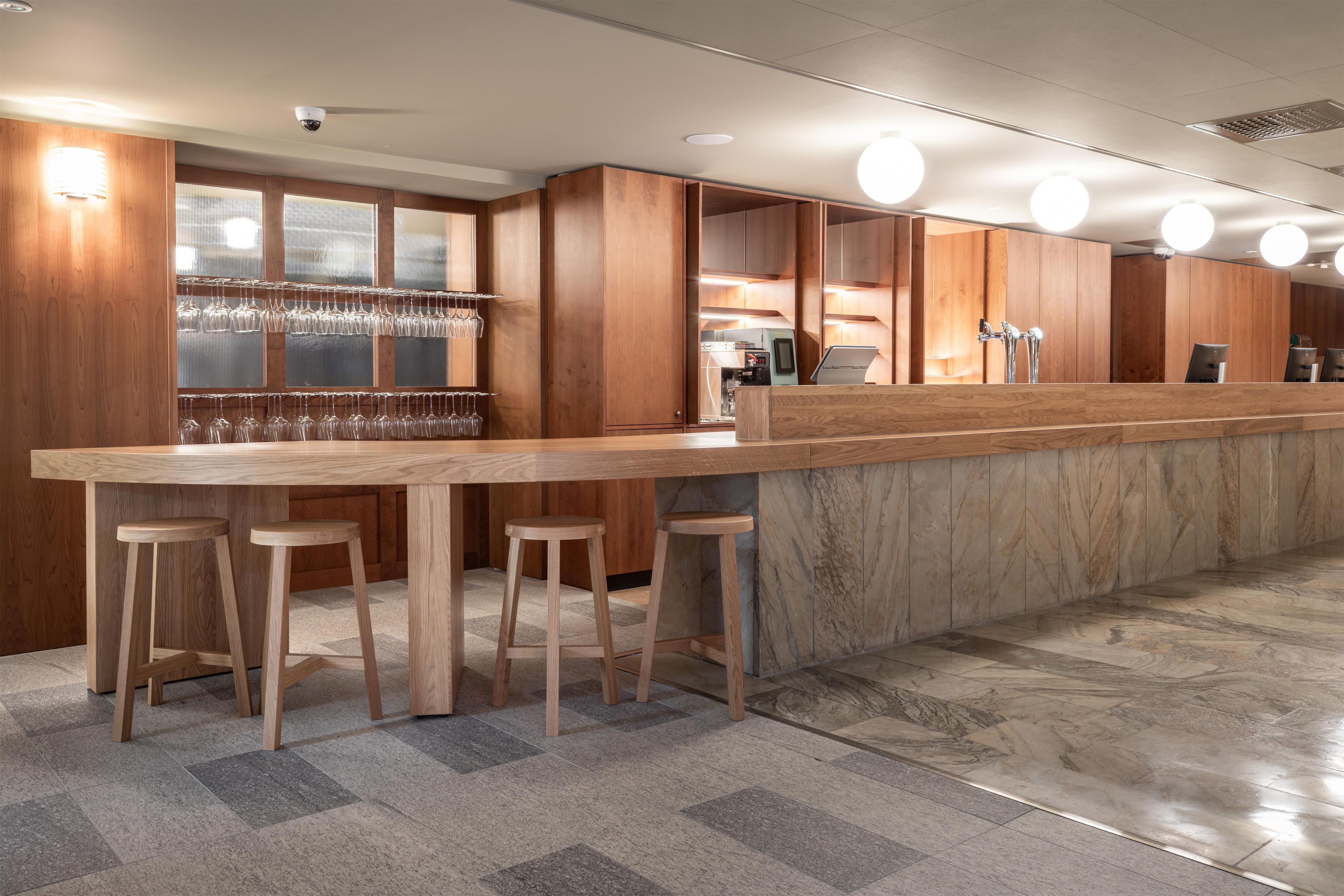 A modern bar area with a wooden counter, bar stools, and a glass wine rack.