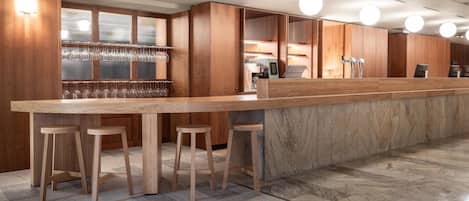 Un área de bar moderna con mostrador de madera, taburetes y una estantería de vidrio para vinos.