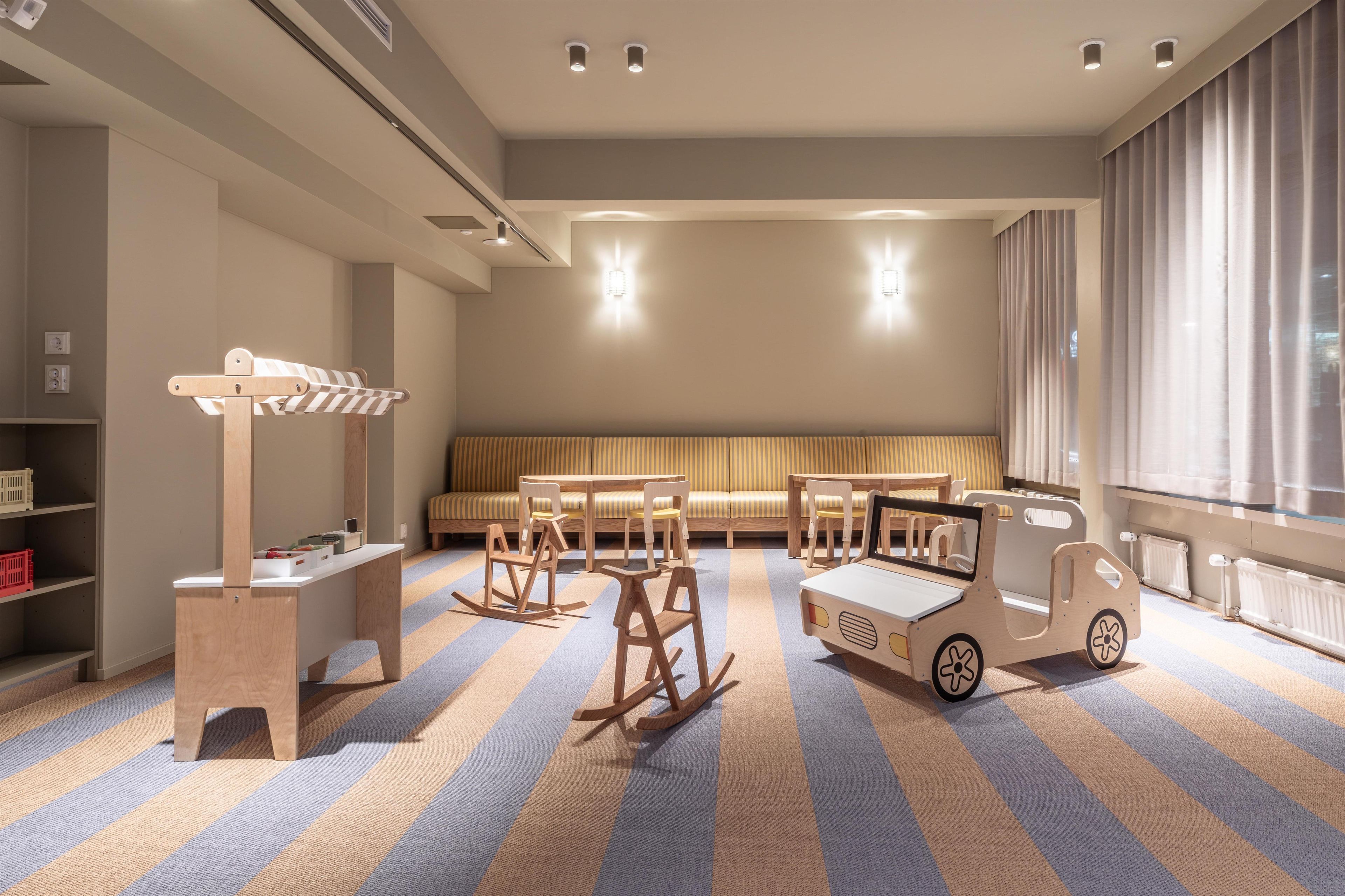 A children's playroom with striped carpet, wooden rocking chairs, a small table, and a toy truck.