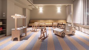 A children's playroom with striped carpet, wooden rocking chairs, a small table, and a toy truck. - Scandic Pohjanhovi (Rovaniemi)