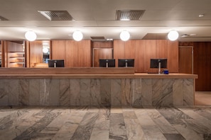 Zona de recepción con suelo de mármol, paneles de madera y tres monitores de ordenador.