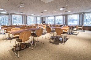 A spacious classroom with wooden tables and chairs, large windows with a view of trees and a bridge, and a carpeted floor. - Scandic Pohjanhovi (Rovaniemi)