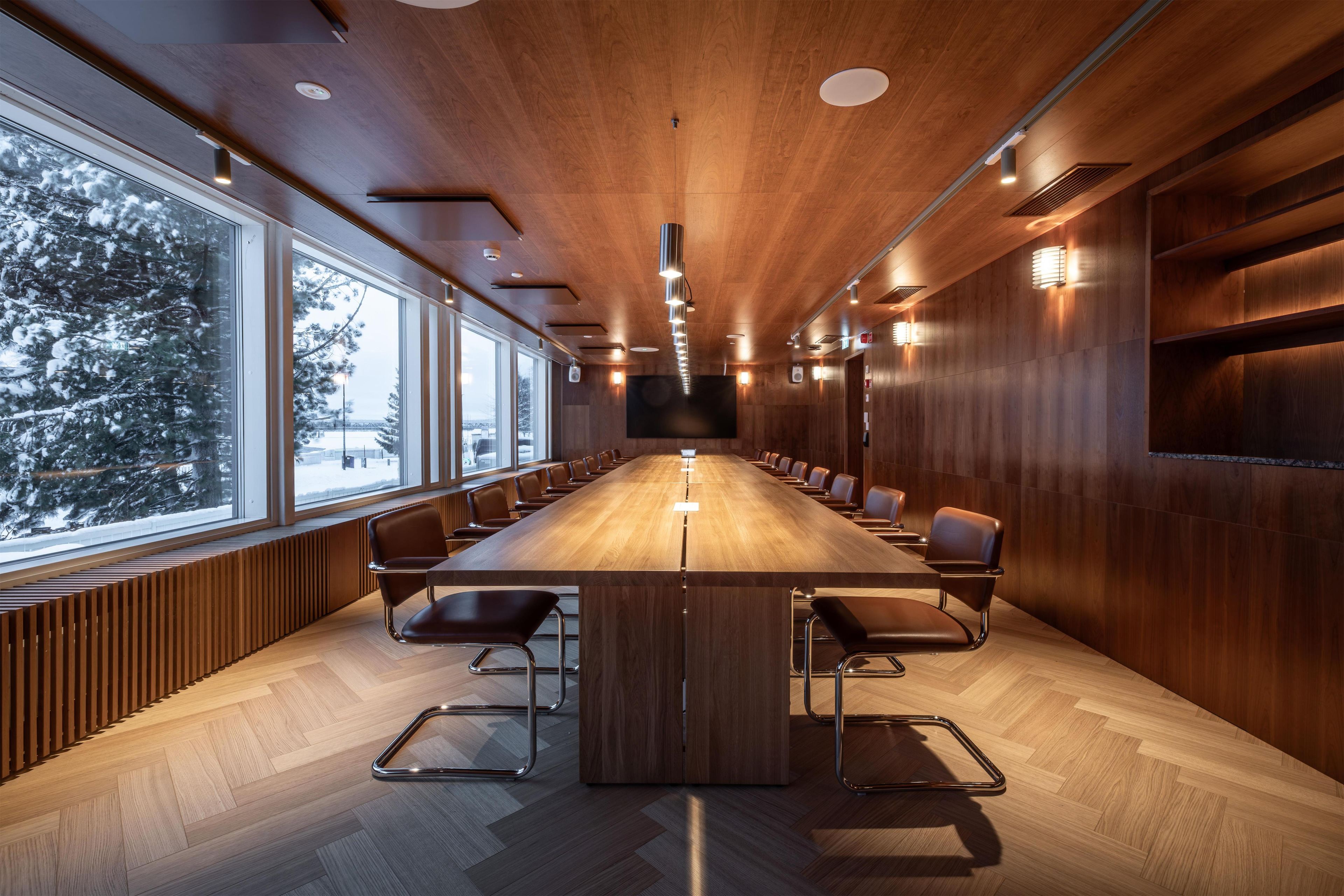 A conference room with a long table, chairs, and a large window overlooking a snowy landscape.
