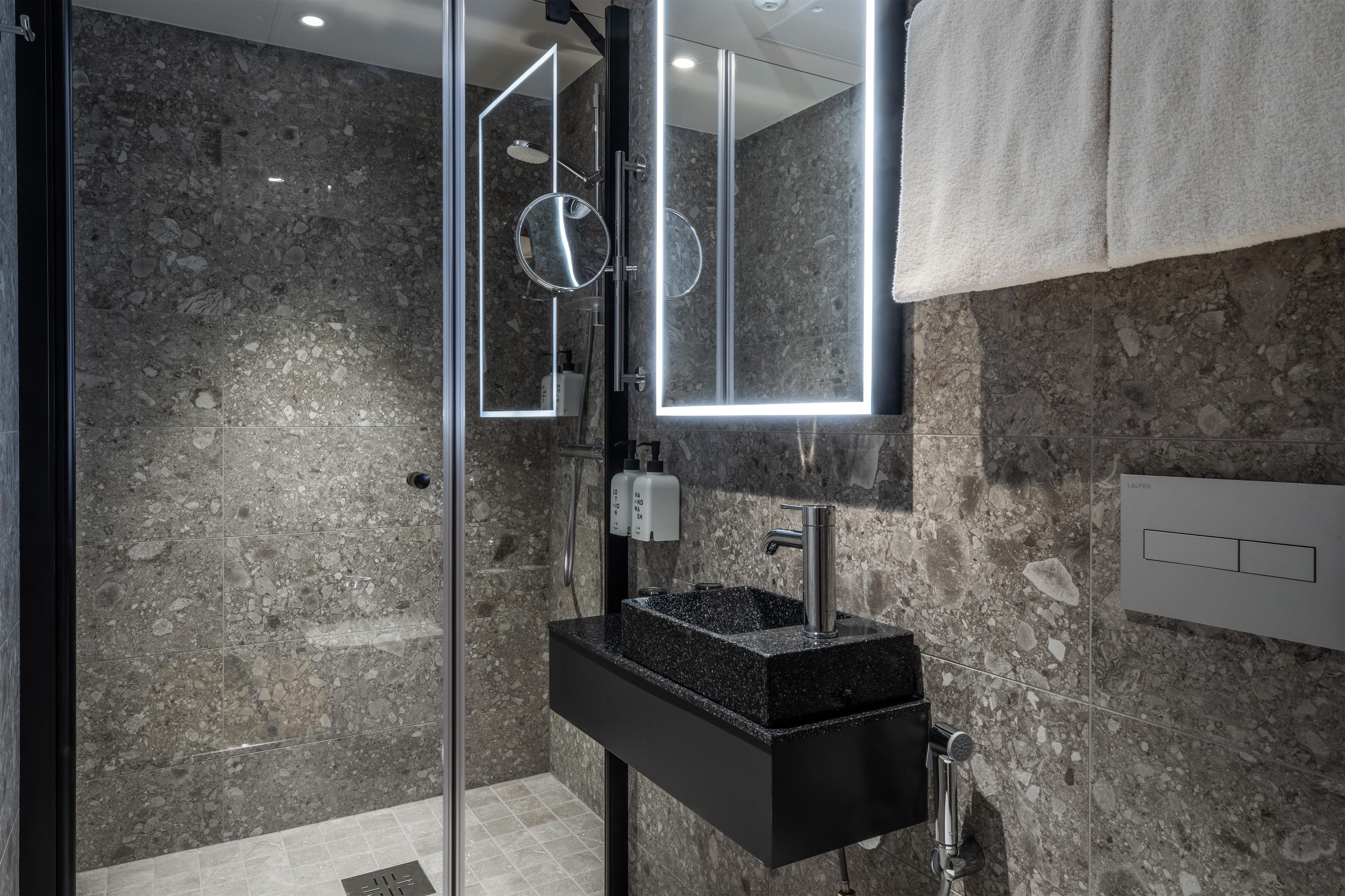 A modern bathroom with a granite sink, a glass shower enclosure, and a mirror with integrated lighting.