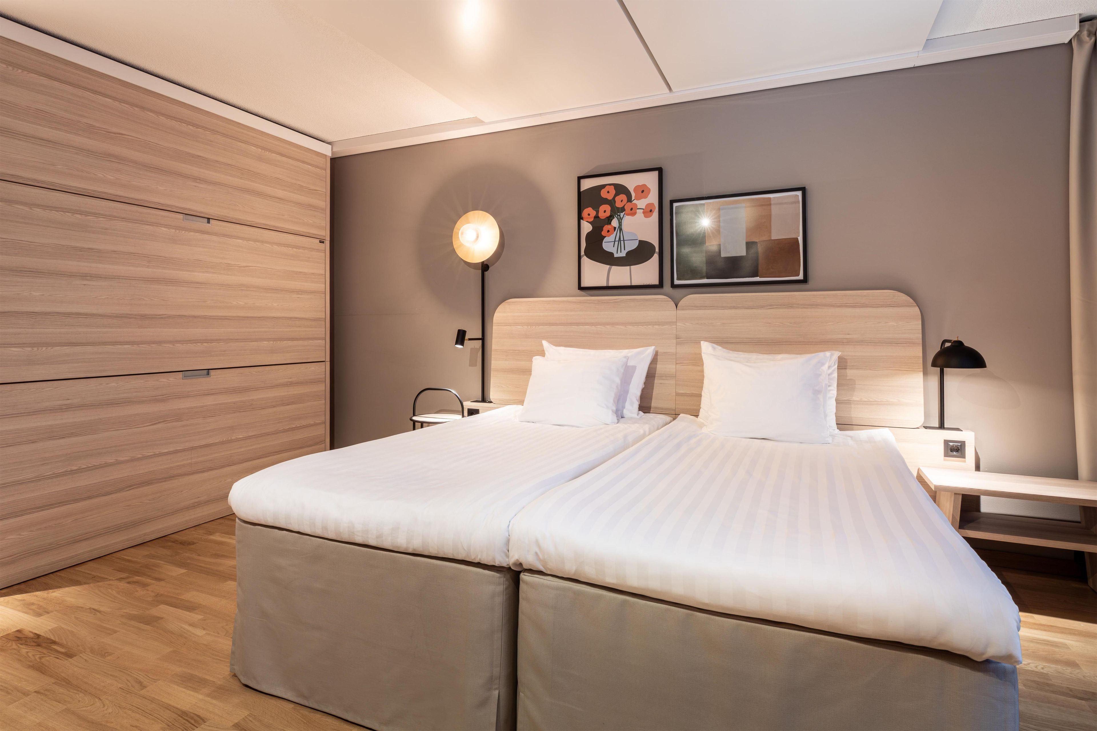 A modern bedroom with a large bed, wooden paneling on the walls, two bedside tables with lamps, and artwork on the wall.