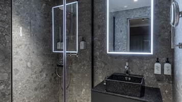 Un baño moderno con encimera de granito, ducha con cerramiento de vidrio y un espejo grande con iluminación integrada.