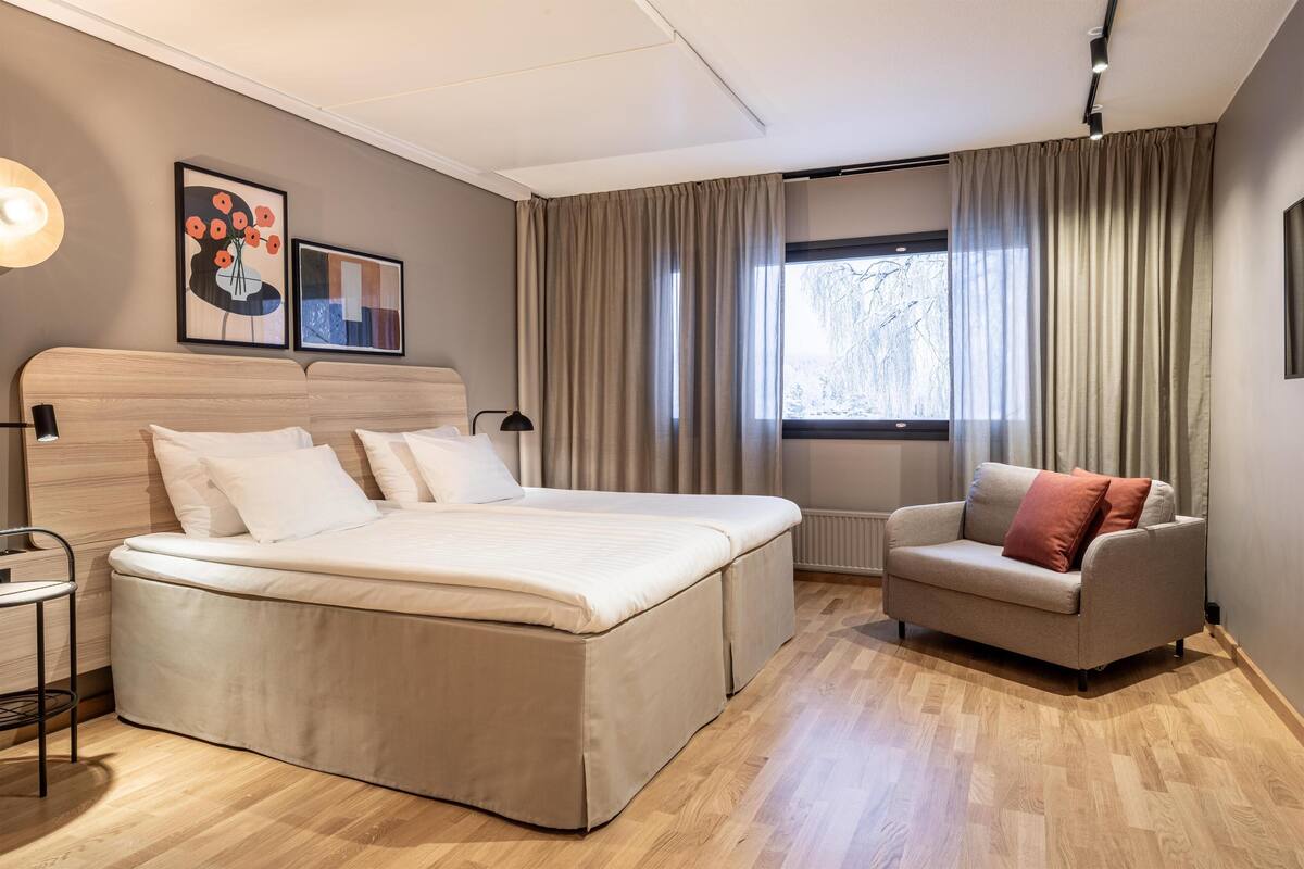 A modern bedroom with a large bed, a sofa, a side table, and a window with curtains.