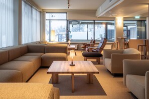 A modern hotel lobby with a large sectional sofa, a wooden coffee table, and several armchairs. Large windows provide a view of the outside. - Scandic Pohjanhovi (Rovaniemi)