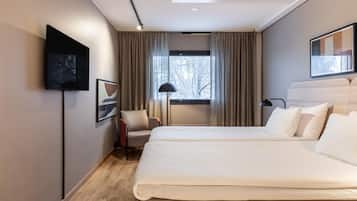 Ett hotellrum med en säng, en stol, en tv och ett fönster med gardiner.