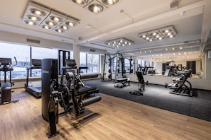 A gym with cardio machines, weightlifting equipment, and large windows offering a view of the outdoors.
