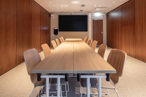A conference room with a long table, chairs, a projector screen, and speakers.