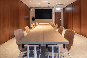 A conference room with a long table, chairs, a projector screen, and speakers.