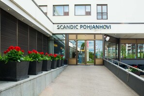 The exterior of a building with the name "SCANDIC POHJANHOVI" above the entrance. There are potted plants with red flowers in front of the entrance. - Scandic Pohjanhovi (Rovaniemi)
