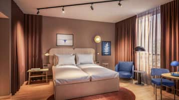 Ett modernt hotellrum med en säng, sängbord, en stol, ett skrivbord och ett stort fönster med gardiner.