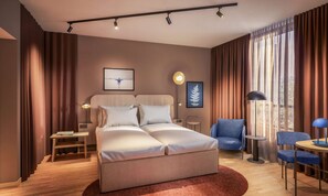 A modern hotel room with a bed, bedside tables, a chair, a desk, and a large window with curtains.