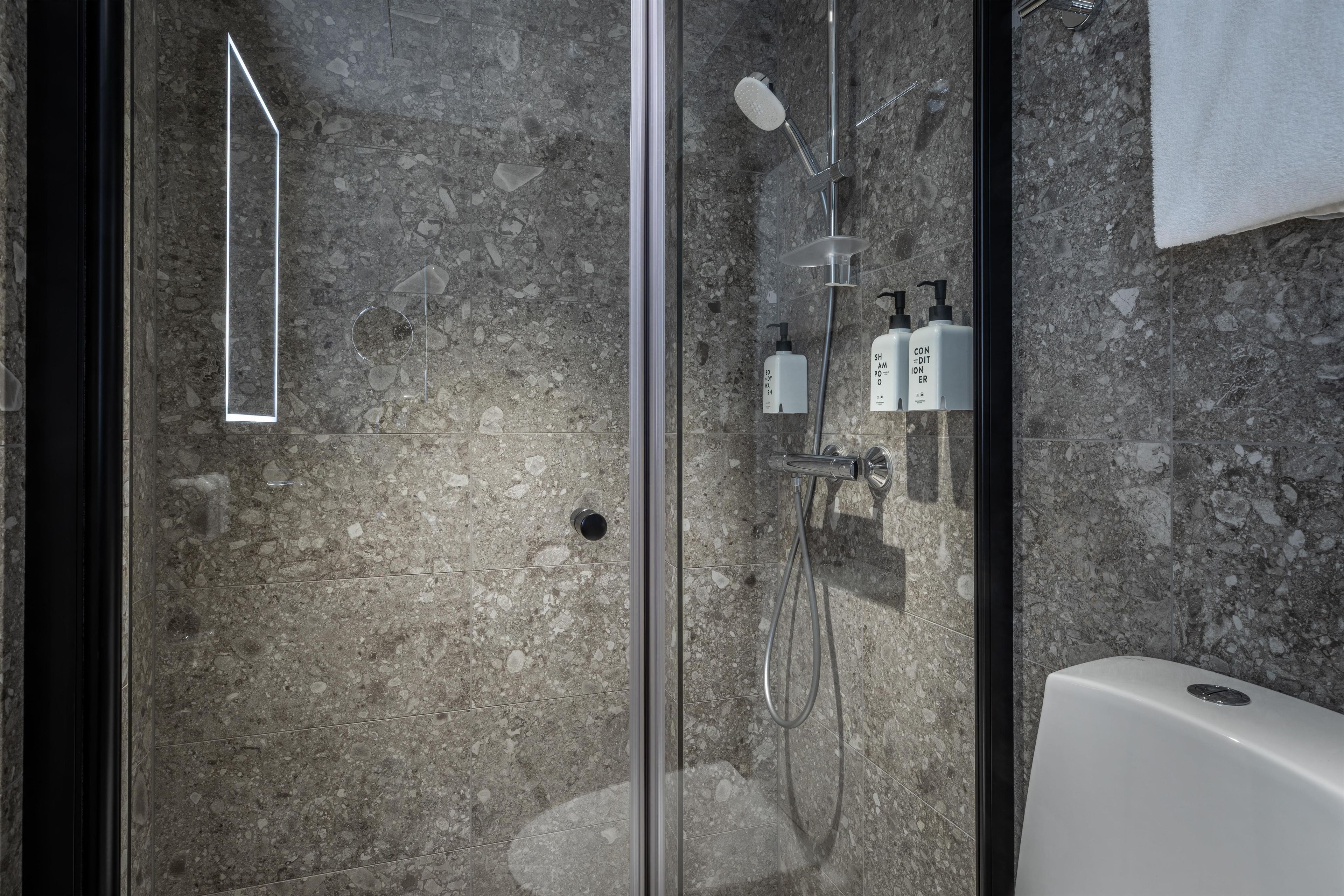 Un baño moderno con ducha de vidrio, pared de mármol y bañera blanca.