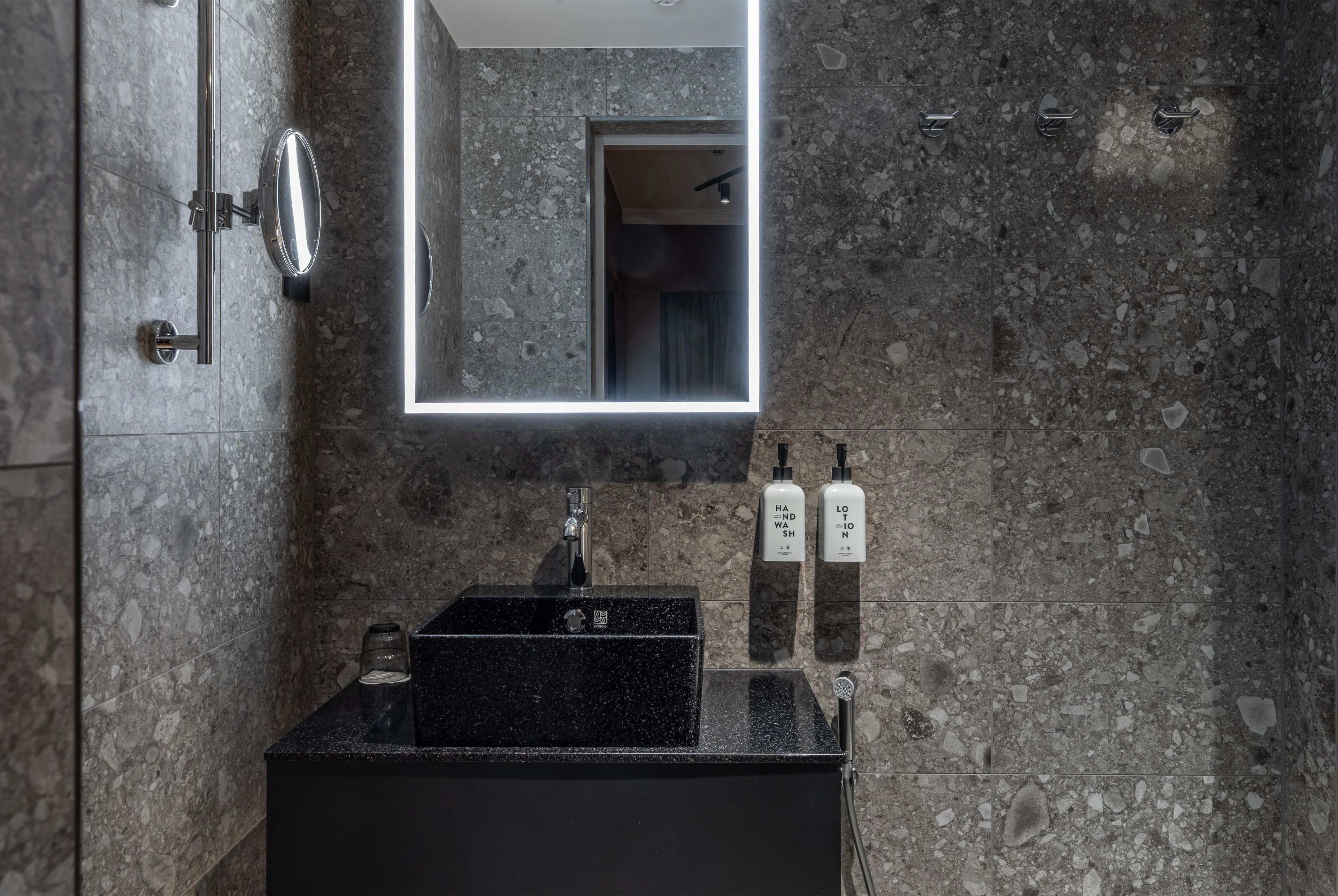 A modern bathroom with a granite countertop, a black sink, and a mirror with a lighted frame.