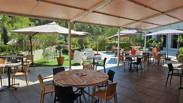 Un espace extérieur aménagé en terrasse, avec des tables et des chaises rondes, des parasols et des plantes en pot.