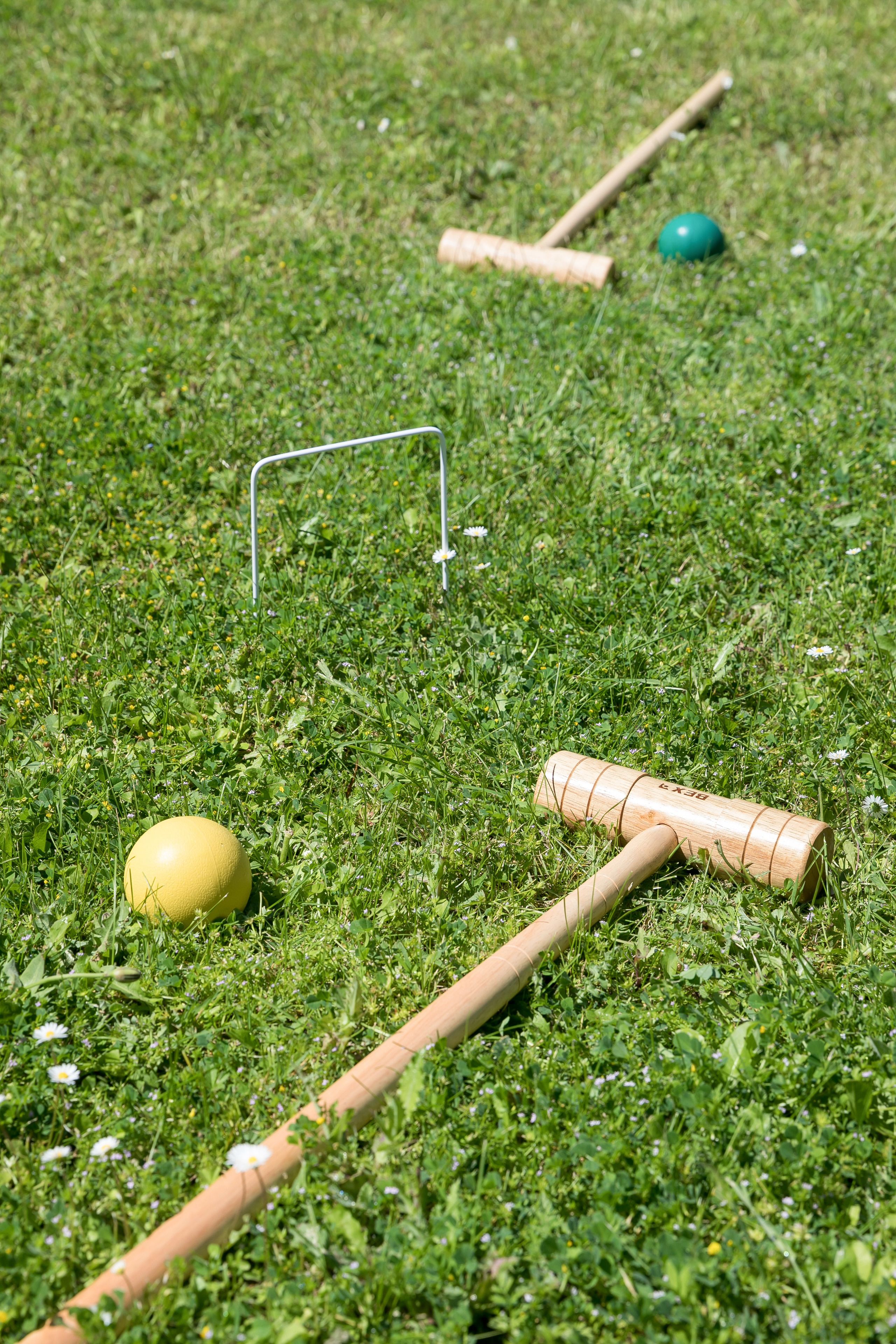 A croquet set on a grassy field with a metal hoop and two wooden mallets.