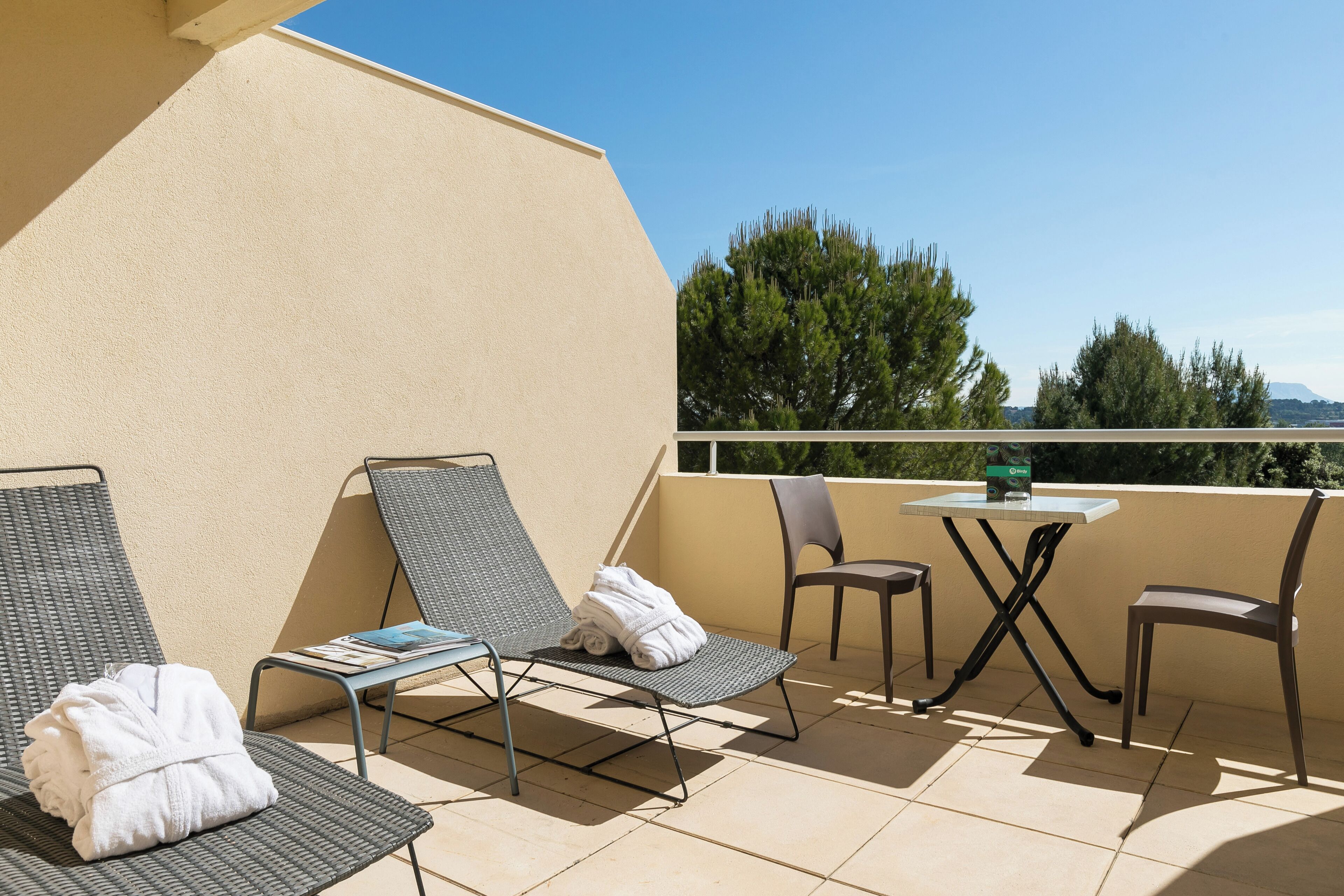 A balcony with two lounge chairs, a small table, and a view of trees and mountains.