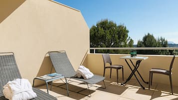 Un balcón con dos sillones, una mesita y vistas a árboles y montañas.