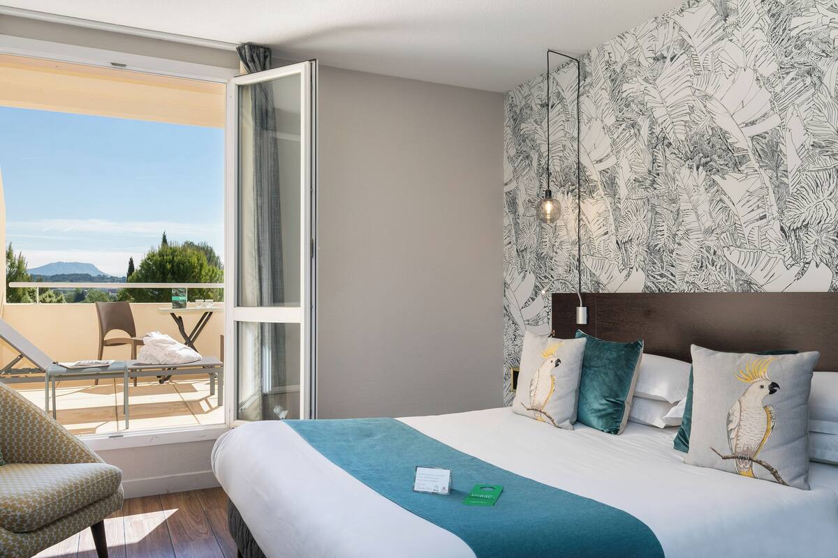 Une chambre d’hôtel avec un grand lit, un balcon avec une chaise et une vue sur les montagnes.