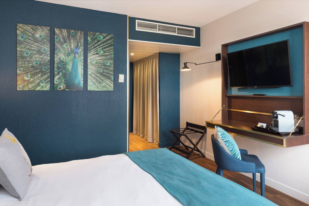 Une chambre d’hôtel comprenant un lit, un bureau avec un téléviseur à écran plat, une chaise et une décoration murale sur le thème du paon.