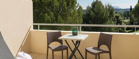 Un balcon avec une table et deux chaises, une serviette posée sur une chaise, et une vue sur des arbres et des collines.
