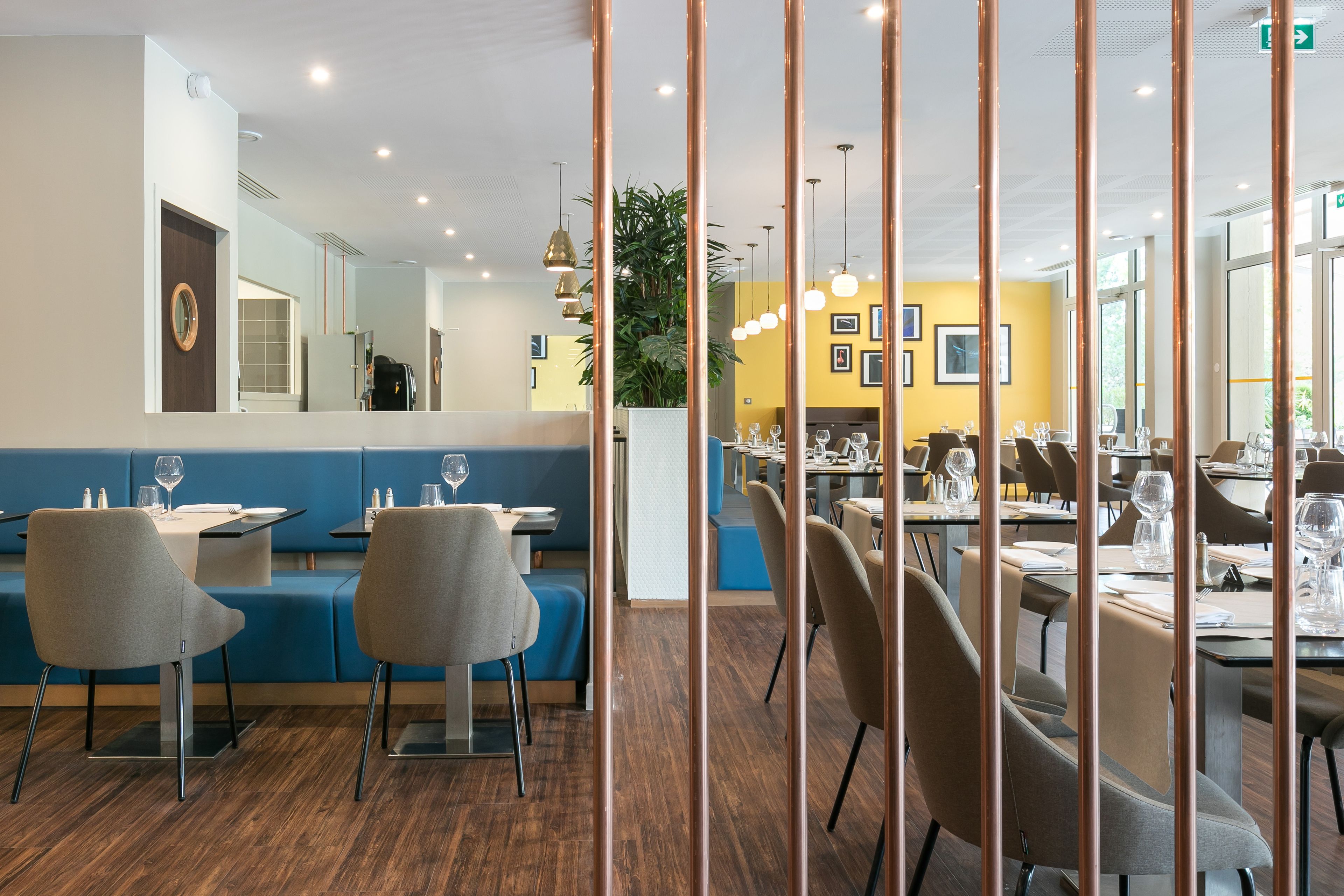 A modern restaurant with blue booths and dining tables, wooden flooring, and a large mirror on the wall.
