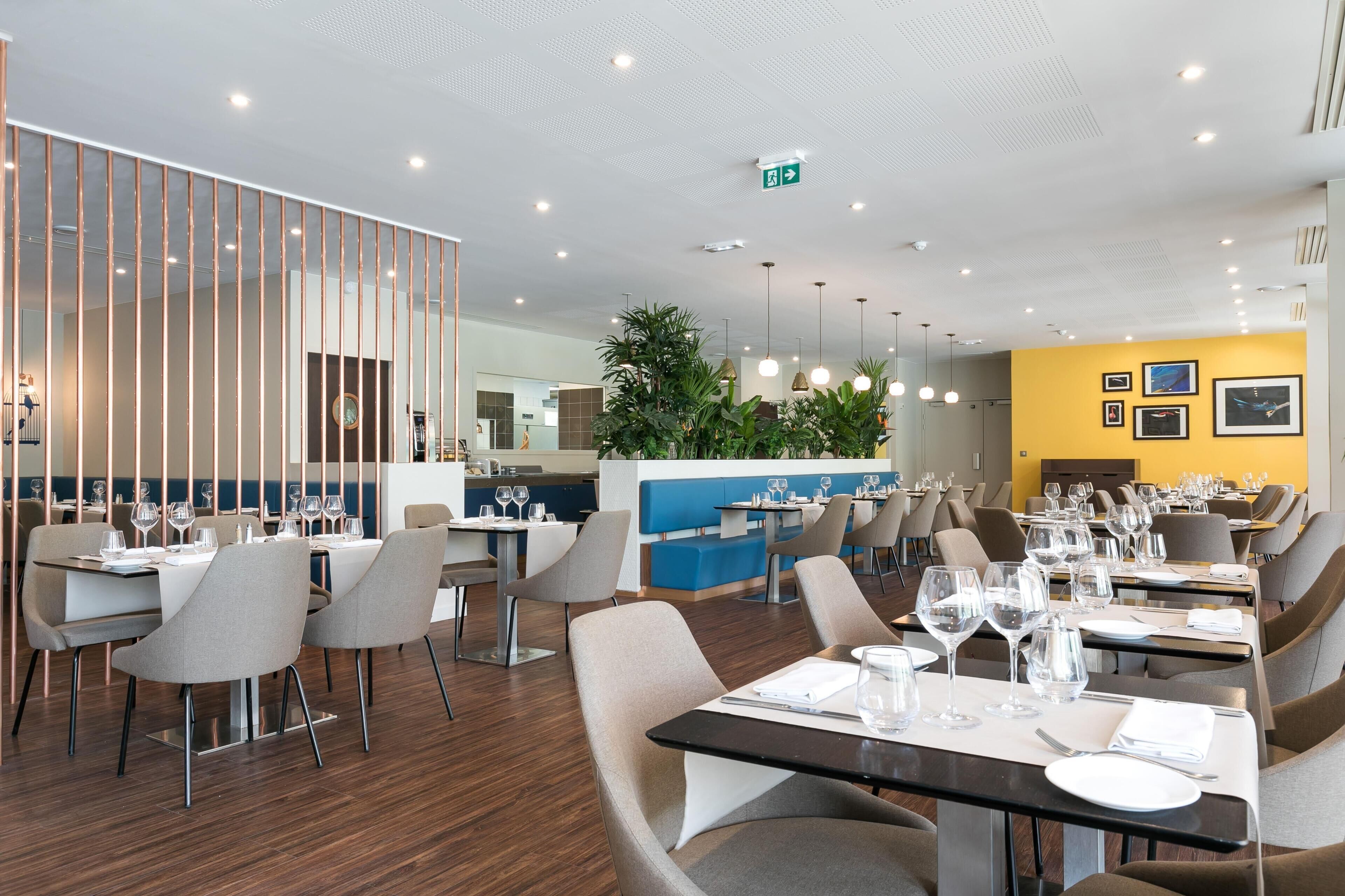 A modern restaurant with wooden flooring, grey and beige chairs, and tables set for dining.