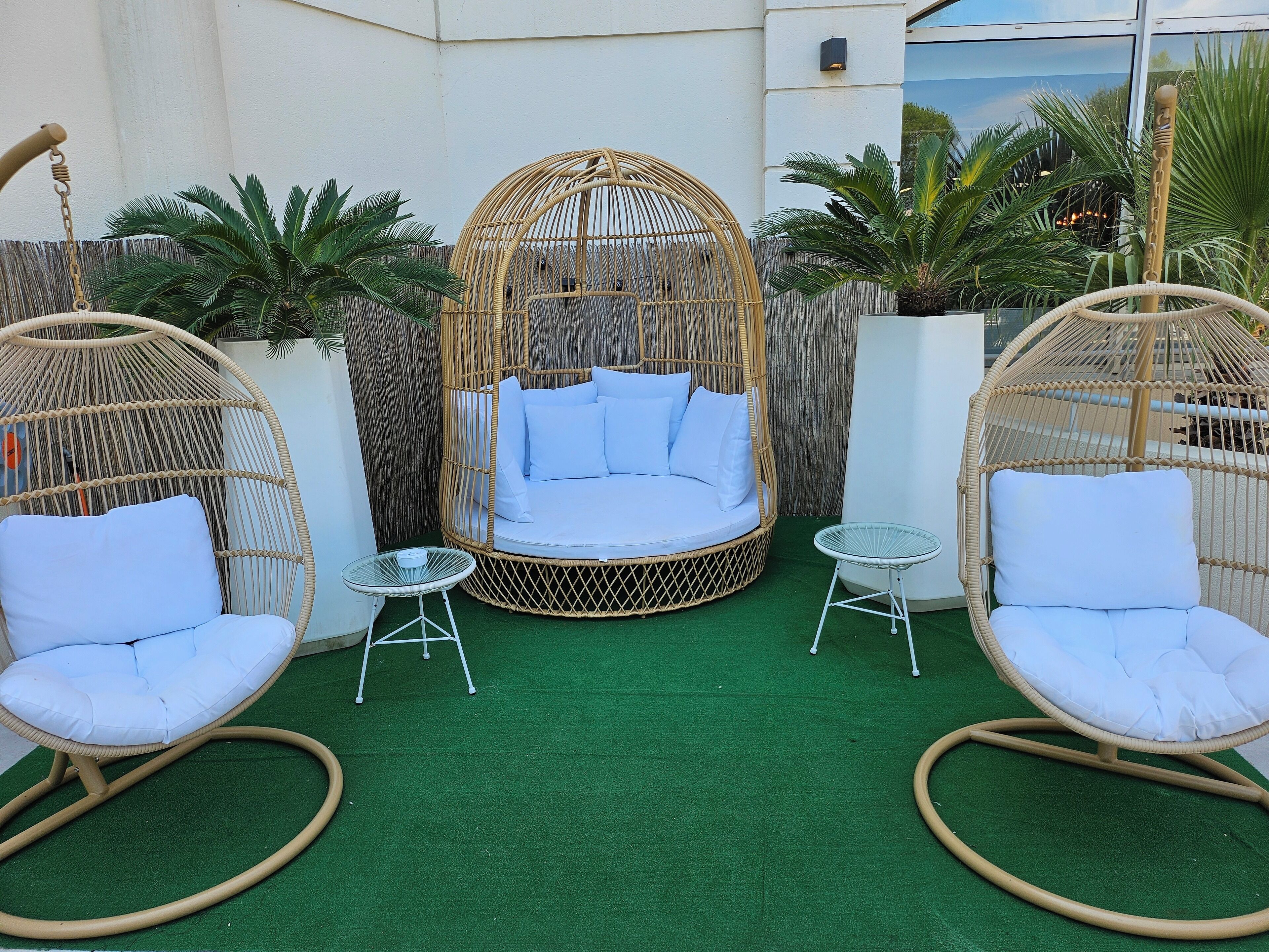 A cozy outdoor seating area with a wicker swing chair, a cushioned bench, and a small round table.
